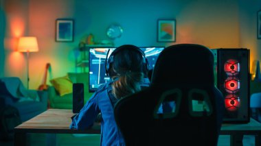 Onun Güçlü Kişisel Bilgisayarda First-Person Shooter Online Video Oyunu Oynayan Bir Oyun Kız Back Shot. Oda ve Pc Renkli Sıcak Neon Led Işıklar var. Evde Rahat Akşam.
