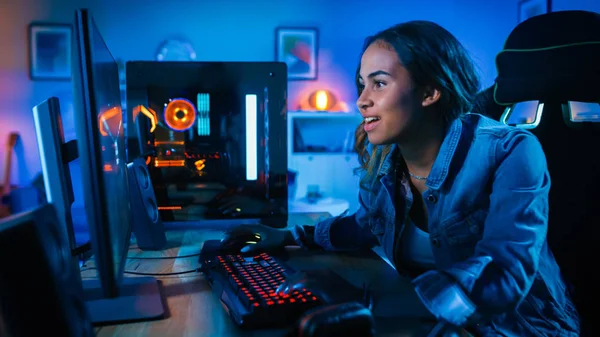 Hermosa y emocionada Chica Negro Gamer está jugando en primera persona Shooter Juego de vídeo en línea en su ordenador. La habitación y la PC tienen luces led de neón coloridas. Acogedora noche en casa . —  Fotos de Stock
