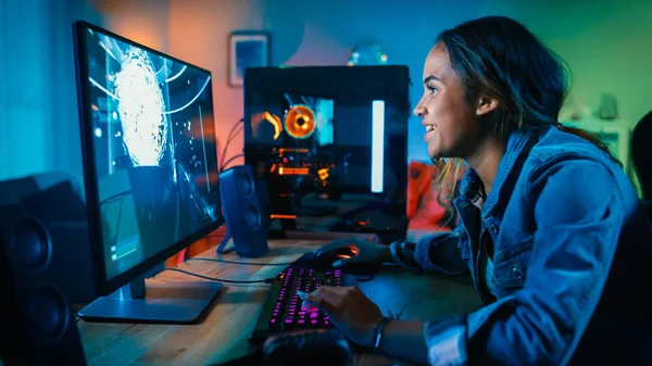 Hermosa y emocionada Chica Negro Gamer está jugando en primera persona Shooter Juego de vídeo en línea en su ordenador. La habitación y el PC tienen luces led de GreenNeon. Acogedora noche en casa . —  Fotos de Stock