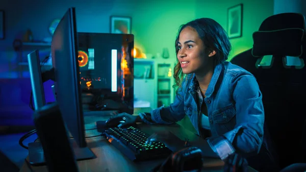 Beautiful and Excited Black Gamer Girl is Playing First-Person Shooter Online Video Game on Her Computer. Room and PC have GreenNeon Led Lights. Cozy Evening at Home.