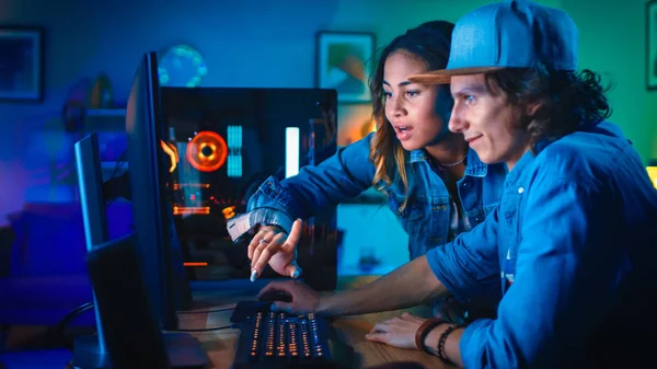 Dos amigos bloggers o una pareja discuten activamente algo en una pantalla de computadora. Pretty Black Girl señala la pantalla y Young Man está de acuerdo con sus ideas creativas. Acogedora habitación está iluminada con luz de neón verde . — Foto de Stock