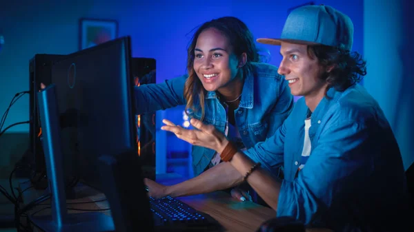 Два друга-блогера или пара активно обсуждают что-то на экране компьютера. Красивая чёрная девушка указывает на экран, и молодой человек соглашается с её творческими идеями. Уютная комната с синим неоновым светом . — стоковое фото