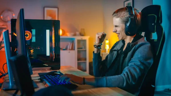 Aufgeregter Spieler, der auf seinem PC in einem Ego-Shooter-Online-Videospiel spielt und gewinnt. Zimmer und PC haben bunte Neon-LED-Lichter. Der junge Mann trägt Kopfhörer. Gemütlicher Abend zu Hause. — Stockfoto