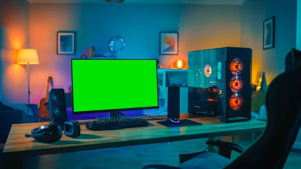 Potente ordenador personal Gamer Rig con Mock Up monitor de pantalla verde se coloca en la mesa en casa. Acogedora habitación con diseño moderno es Lit con luz cálida y neón . — Foto de Stock