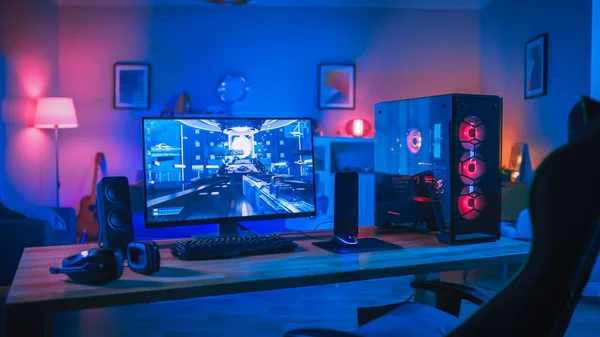 Leistungsstarkes PC-Gamer-Rig mit Ego-Shooter-Spiel auf dem Bildschirm. Monitor steht zu Hause auf dem Tisch. gemütliches Zimmer mit modernem Design ist mit rosa Neonlicht beleuchtet. — Stockfoto