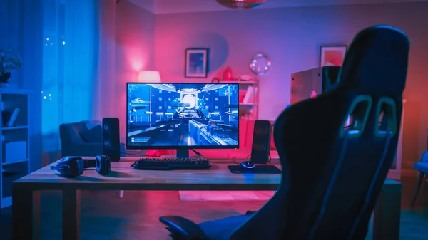 Powerful Personal Computer Gamer Rig with First-Person Shooter Game on Screen. Monitor Stands on the Table at Home. Cozy Room with Modern Design is Lit with Pink Neon Light. — Stock Photo, Image