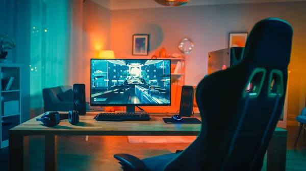 Ekranda First-Person Shooter Oyunu ile Güçlü Kişisel Bilgisayar Gamer Rig. Monitör Evde Masada Duruyor. Modern Tasarımlı Rahat Oda Sıcak ve Neon Işıkla Aydınlatıldı.