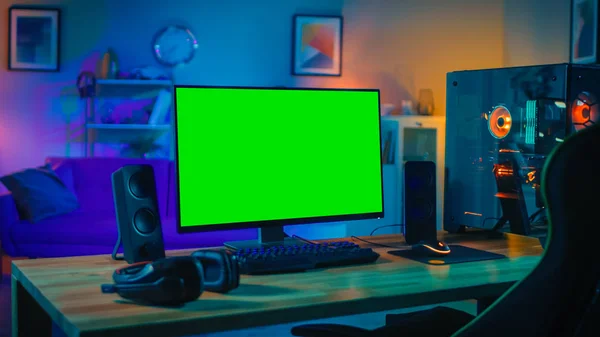 Potente ordenador personal Gamer Rig con Mock Up monitor de pantalla verde se coloca en la mesa en casa. Acogedora habitación con diseño moderno es Lit con luz cálida y neón . — Foto de Stock