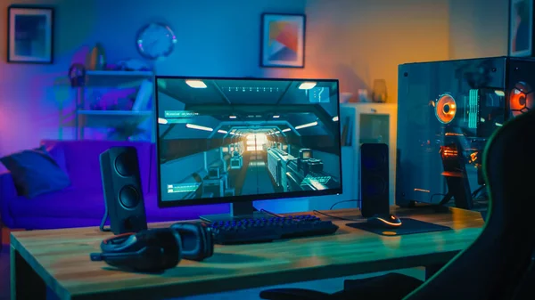 Leistungsstarkes PC-Gamer-Rig mit Ego-Shooter-Spiel auf dem Bildschirm. Monitor steht zu Hause auf dem Tisch. gemütliches Zimmer mit modernem Design ist mit warmem Neonlicht beleuchtet. — Stockfoto