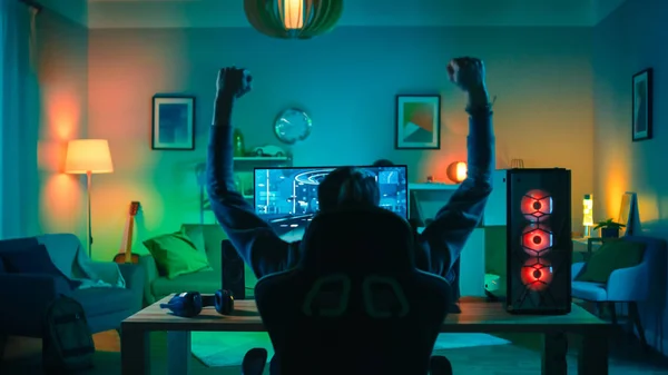 Back Shot of a Gamer Jogando e vencendo em primeira pessoa Shooter Online Video Game em seu poderoso computador pessoal. O quarto e o PC têm luzes conduzidas de néon verde. Noite aconchegante em casa . — Fotografia de Stock