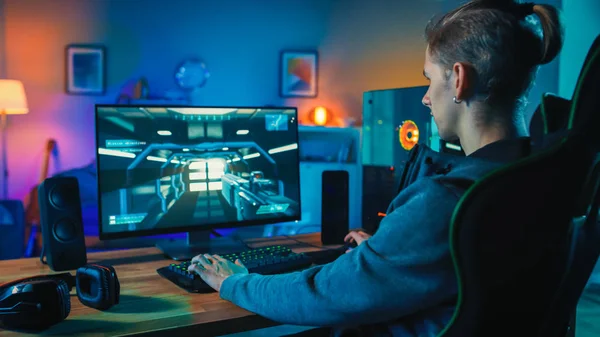 Back shot van een gamer spelen first-person shooter online video game op zijn krachtige personal computer. Kamer en PC hebben warme kleurrijke Neon LED-verlichting. Gezellige avond thuis. — Stockfoto