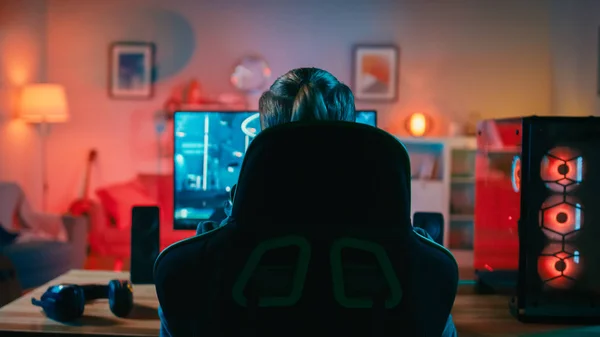 Back Shot of a Gamer Jogando em Primeira Pessoa Shooter Online Video Game em Seu Poderoso Computador Pessoal. Quarto e PC têm luzes LED de néon coloridas. Noite aconchegante em casa . — Fotografia de Stock