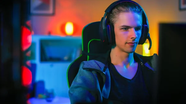 Gamer w zestawie słuchawkowym z mikrofonem gra online wideo gra na jego komputerze osobistym. Daje rozkazy innym graczom. Pokój i komputer mają kolorowe Neon LED Lights. Przytulny wieczór w domu. — Zdjęcie stockowe