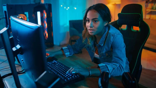 Krásná a vzrušená černá Gamer Girl hraje online videohru na jejím osobním počítači. V místnosti a počítači jsou barevné teplé neonové indikátory LED. Útulný večer doma. — Stock fotografie