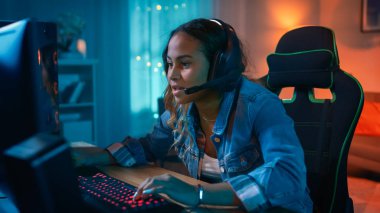Mikrofon Onun Kişisel Bilgisayar online video oyunu oynamak ile Kulaklık Heyecanlı ve Odaklı Gamer Girl. Diğer Oyuncularla Konuşuyor. Oda ve Pc Renkli Sıcak Neon Led Işıklar var. Evde Rahat Akşam.