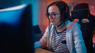 Onun Kişisel Bilgisayar da Bir Mikrofon Playing Online Video Oyunu ile Kulaklık Heyecanlı Gamer Girl. Diğer Oyuncularla Konuşuyor. Oda ve Pc Renkli Sıcak Neon Led Işıklar var. Evde Rahat Akşam.