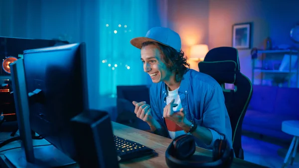 Guapo joven sorprendido y emocionado viendo un video de acción en una computadora. Él es feliz y celebrando. Screen agrega reflexiones a su rostro. Acogedora habitación está iluminada con luz cálida . —  Fotos de Stock