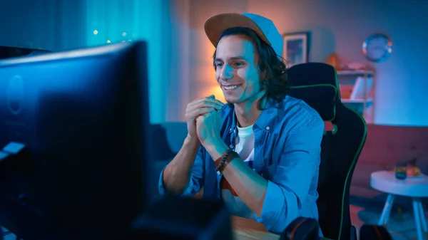 Knap opgewonden jonge man kijken naar een actie video op een computer. Hij is gelukkig. Gezellige kamer verlicht met warm licht. — Stockfoto