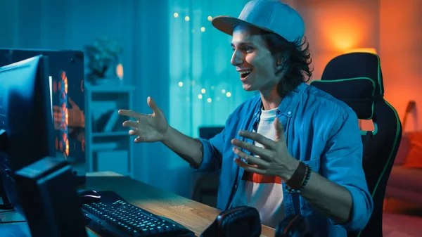 Guapo joven sorprendido y emocionado viendo un video de acción en una computadora. Él es feliz y celebrando. Screen agrega reflexiones a su rostro. Acogedora habitación está iluminada con luz cálida . — Foto de Stock