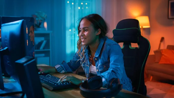 Mooie verrast en opgewonden Jong zwart meisje kijken naar actie video op een computer. Ze heeft donker haar en bruine ogen. Scherm voegt reflecties toe aan haar gezicht. Gezellige kamer verlicht met warm licht. — Stockfoto