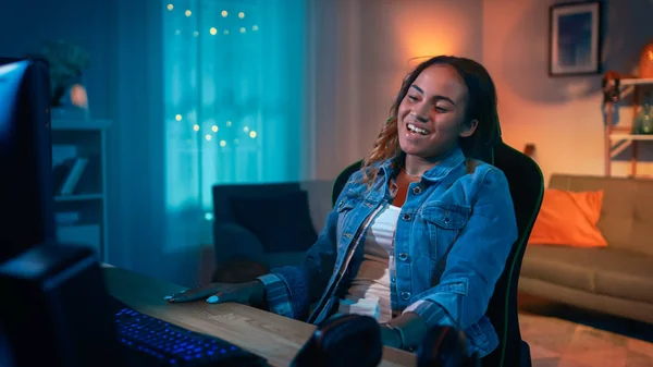 Linda menina negra surpreso e animado assistindo vídeo de ação em um computador. Ela tem cabelo escuro e olhos castanhos. Screen Adiciona Reflexões ao Seu Rosto. Quarto acolhedor é lit com luz quente . — Fotografia de Stock