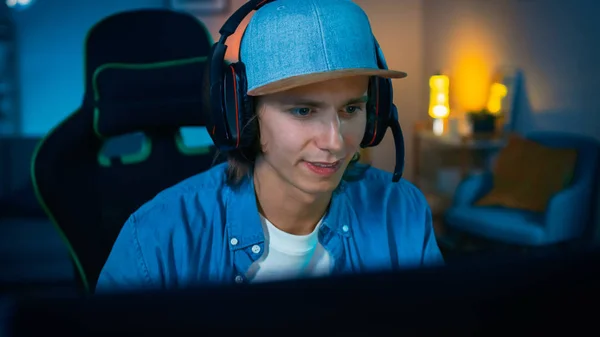 Streamer Popular está jogando videogame online em seu computador pessoal. O quarto e o PC têm luzes conduzidas quentes coloridas do néon. Young Man está usando fones de ouvido com um microfone. Noite aconchegante em casa . — Fotografia de Stock