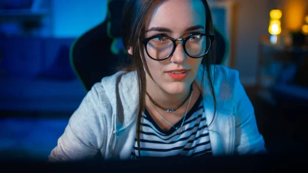 Emocionado e Pretty Gamer Girl in Glasses está jogando videogame online em seu computador pessoal. O quarto e o PC têm luzes conduzidas quentes coloridas do néon. Noite aconchegante em casa . — Fotografia de Stock