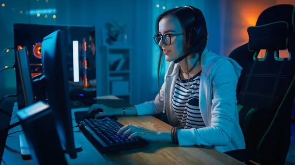 Podekscytowany Gamer Girl w zestawie słuchawkowym z mikrofonem gra online wideo gra na jej komputerze osobistym. Rozmawia z innymi graczami. Pokój i komputer mają kolorowe ciepłe Neon LED Lights. Przytulny wieczór w domu. — Zdjęcie stockowe
