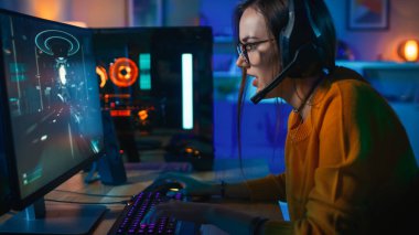 Onun Bilgisayarda Shooter Online Video Oyunu Playing Bir Mikrofon ile Gözlük ve Kulaklık Pretty ve Heyecanlı Gamer Girl. Oda ve Pc Renkli Neon Led Işıklar var. Evde Rahat Akşam.
