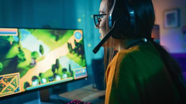 Heyecanlı ve Konsantre Gamer Girl Gözlük ve Kulaklık bir Mikrofon Onun Kişisel Bilgisayar da Online Strateji Video Oyunu Playing ile. Oda ve Pc Renkli Sıcak Neon Led Işıklar var. Evde Rahat Akşam.