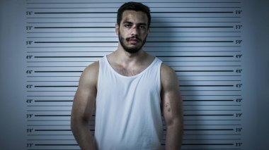 Bir Polis Karakolu'nda Tutuklanan Dayak Adam Front View Mugshot için Pozlar. O Singlet giyer, Ağır Çürük olduğunu. Arka Planda Yükseklik Grafiği. Koyu Soğuk Işıklar ve Vignette Filtre ile Çekim.