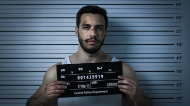 Bir Polis Karakolunda Tutuklanan Dövülmüş Adamın Yakın Çekimi Ön Görünüm Mugshot'a Poz Veriyor. O Singlet giyer, Ağır Çürük ve Placard tutar. Arka Plandaki Yükseklik Grafiği.