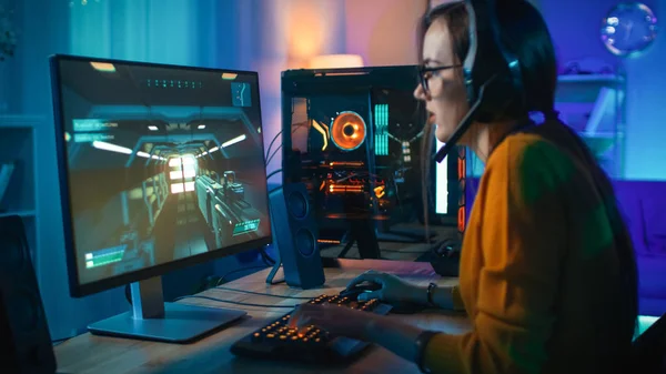 Excited Gamer Girl in Headset with a Mic Playing Online Video Game. Focus is on Her Personal Computer. Room and PC have Colorful Warm Neon Led Lights. Cozy Evening at Home. — Stock Photo, Image