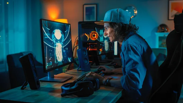 Играть в онлайн-игру первоклассного стрелка на своем мощном персональном компьютере. Номер и компьютер оснащены разноцветными неоновыми лампами. Молодой человек носит кепку. Уютный вечер дома . — стоковое фото