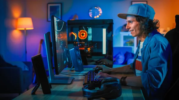 Professionele gamer spelen first-person shooter online video game op zijn krachtige personal computer. Kamer en PC hebben kleurrijke Neon LED-lampjes. Jonge man draagt een pet. Gezellige avond thuis. — Stockfoto