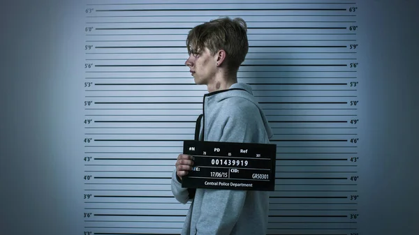 In a Police Station Arrested Drug Addict Teenage Posing for a Side View Mugshot. He is Heavily Bruised. Height Chart in the Background. — Stock Photo, Image
