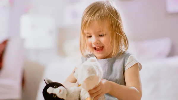 In the Childrens Room: Cute Happy Little Girl seduta su un tappeto e che gioca con i peluche. Soggiorno soleggiato con bambino Divertimento . — Foto Stock