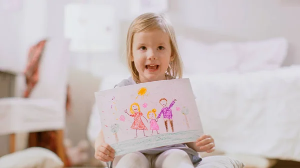 Linda joven sentada en almohadas y muestra el dibujo de su familia. Sala de estar soleado . — Foto de Stock