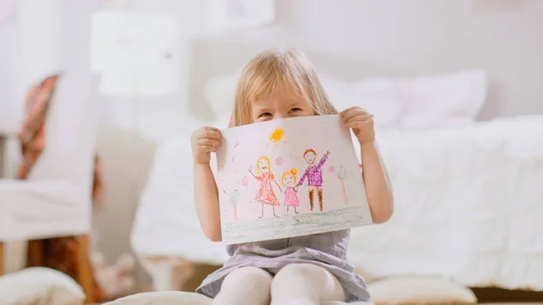 베개에 앉아 귀여운 어린 소녀와 쇼 그림 의 그녀의 가족과 숨기기 뒤에.. — 스톡 사진