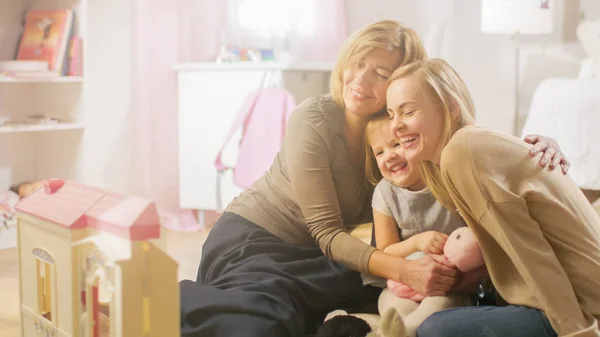Bestemor, mor og hennes lille søte datter har en stor klem. De er på et barnerom som er rosa og fullt av leker. . – stockfoto