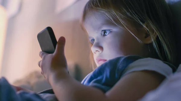 Primo piano colpo di una bambina carina orologi cartoni animati su uno Smartphonein un letto . — Foto Stock