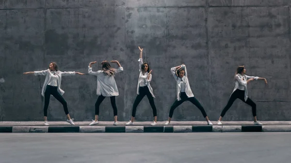 Multiple Exposure Shot of a Cool Cloned Giovane donna bionda con capelli lunghi posa in tre pose di danza su una strada accanto a un grande muro di cemento. Indossa una camicia bianca a righe e jeans scuri. . — Foto Stock