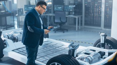 Otomotiv Tasarım Mühendisi Tablet üzerinde elektrikli araba şasi prototipteknik çizim bakıyor. İnovasyon Laboratuvarı Nda Tesis Konsept Araç Çerçevesi Tekerlekler, Motor ve Akü.