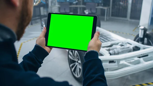 Ingenjör med glasögon och skägg skannar elbil chassi prototyp med hjul, batterier och motor med en förstärkt verklighet programvara på en Tablet PC i ett högteknologiskt utvecklingslaboratorium. — Stockfoto