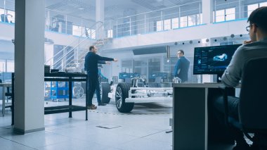 Otomotiv Tasarım Mühendisleri Elektrikli Araç Şasi Prototipi Üzerinde Çalışırken ve Cad Yazılımı ile Pc Kullanırken Konuşuyorlar. Yenilikçi Laboratuvar Tesisi Konsept Araç Çerçevesi Jantlar, Süspansiyon Içerir.