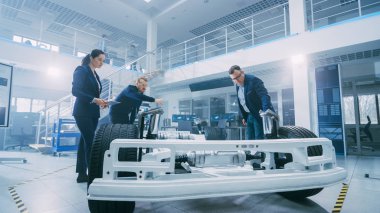 Otomotiv Tasarım Mühendisleri Elektrikli Araç Şasi Prototipi Üzerinde Çalışırken Konuşuyor. Yenilik Laboratuvarı Nda Tesis Konsept Araç Çerçevesi Tekerlekler, Süspansiyon, Motor ve Akü.