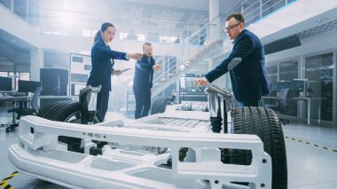 Otomotiv Tasarım Mühendisleri Elektrikli Araç Şasi Prototipi Üzerinde Çalışırken Konuşuyor. Yenilik Laboratuvarı Nda Tesis Konsept Araç Çerçevesi Tekerlekler, Süspansiyon, Motor ve Akü.