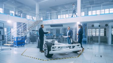Otomotiv Tasarım Mühendisleri Elektrikli Araç Şasi Prototipi Üzerinde Çalışırken Konuşuyor. Yenilik Laboratuvarı Nda Tesis Konsept Araç Çerçevesi Tekerlekler, Süspansiyon, Motor ve Akü.