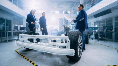 Otomotiv Tasarım Mühendisleri Elektrikli Araç Şasi Prototipi Üzerinde Çalışırken Konuşuyor. Yenilik Laboratuvarı Nda Tesis Konsept Araç Çerçevesi Tekerlekler, Süspansiyon, Motor ve Akü.