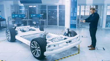 Gözlük ve Sakallı Mühendis, Yüksek Teknoloji Geliştirme Laboratuvarında Tablet Bilgisayarda Artırılmış Gerçeklik Yazılımı ile Tekerlekler, Piller ve Motor ile Elektrikli Araba Şasi Prototipini Tarıyor.